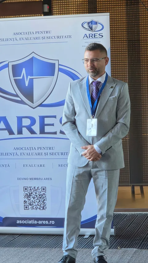 Participant în costum gri deschis, în fața bannerului ARES