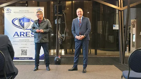 Doi participanți în fața sălii, lângă bannerul Forumului ARES