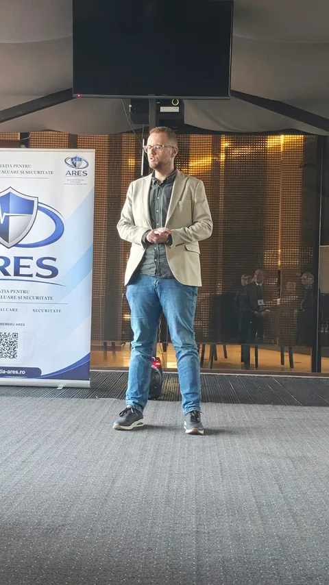 Participant în sacou bej, în timpul unei intervenții lângă bannerul ARES