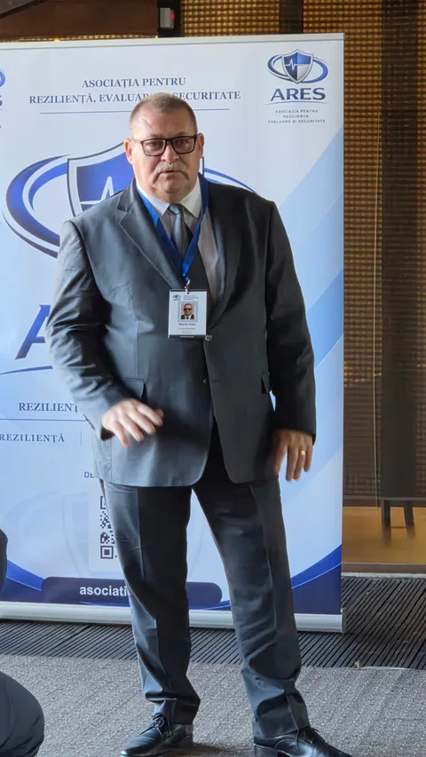Participant cu ochelari și sacou închis la culoare, lângă bannerul ARES